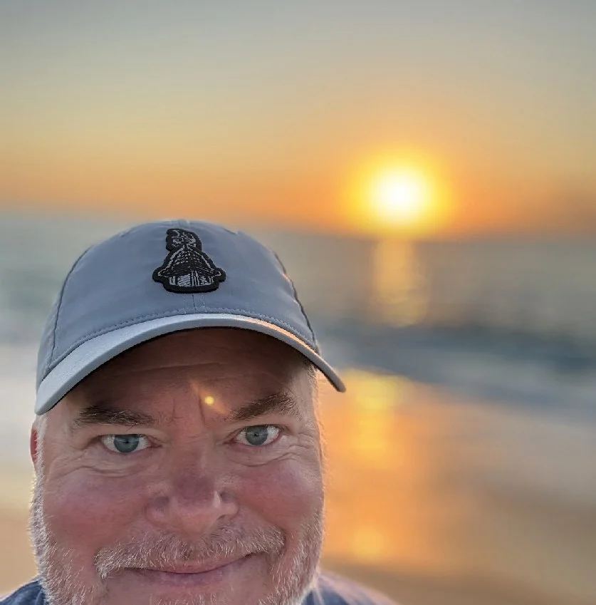 George Jackson smiling in a ball cap on the beach at sunset
